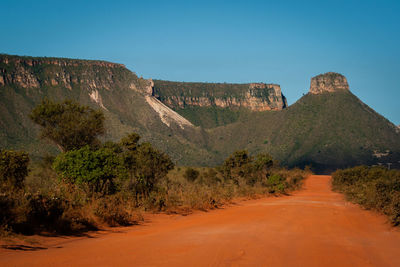 Road amidst rocks and trees against clear blue sky