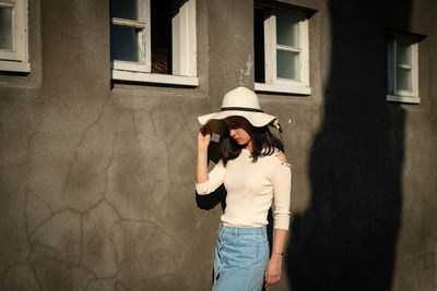 Woman wearing hat while standing by wall