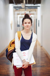 Portrait of woman holding papers while standing in corridor
