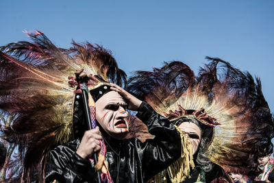 Low angle view of people wearing mask against sky on sunny day