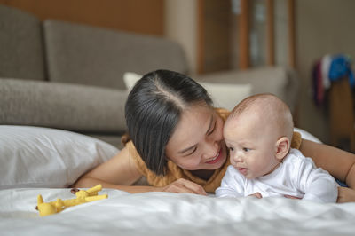 Smiling mother playing with baby son on bed at home