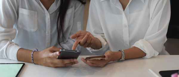 Midsection of colleagues using smart phone sitting at office