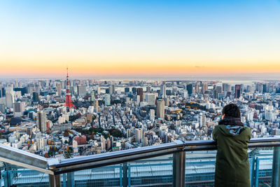 Woman looking at cityscape against sky during sunset