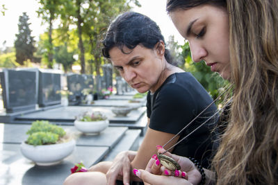 Mother and her daughter in grief, holding a flower and mourning a deceased loved one on cemetery