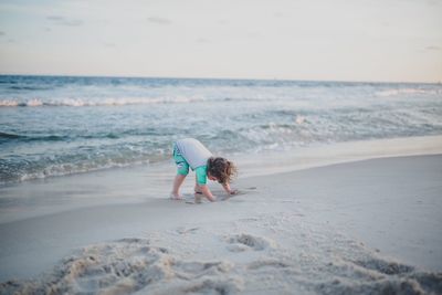 Boy playing with sand at beach against sky