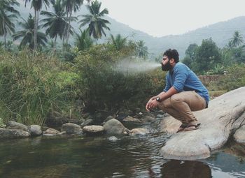 Man spraying water from mouth by river