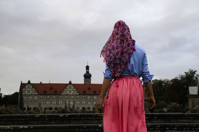 Rear view of woman standing by building against sky