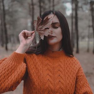 Portrait of young woman holding autumn leaf outdoors