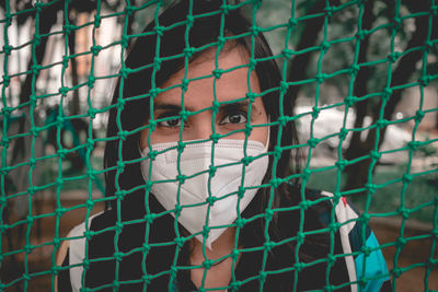 Portrait of woman wearing flu mask standing against net outdoors