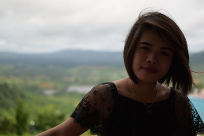 Portrait of smiling woman against cloudy sky