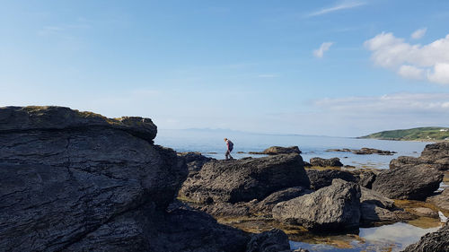 Man walking on rock by sea against sky