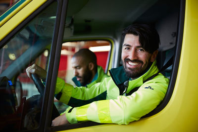 Portrait of smiling male paramedic with coworker driving ambulance in parking lot