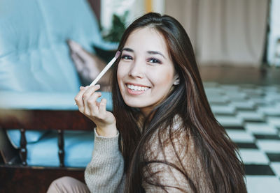 Portrait of smiling young woman holding make-up brush while sitting at home