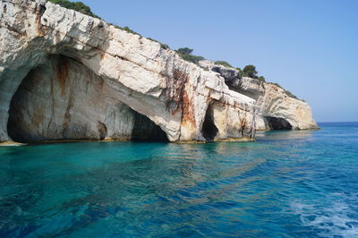 Rock formation by sea against clear blue sky