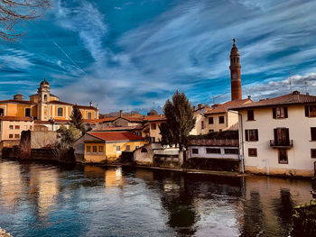 Buildings by river against sky in city