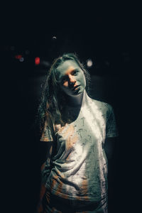 Portrait of young woman standing against black background