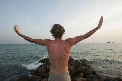 Rear view of shirtless man standing by sea against sky