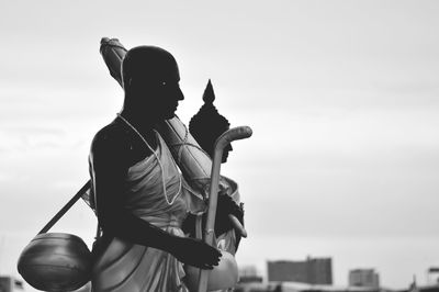 Rear view of man holding sculpture against sky