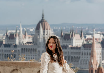 Portrait of beautiful young woman on balcony overlooking hungarian parliament in budapest, hungary