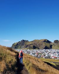 Rear view of woman walking on mountain trail against clear blue sky