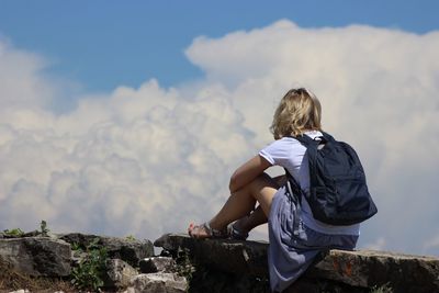 Rear view of man sitting on rock against sky