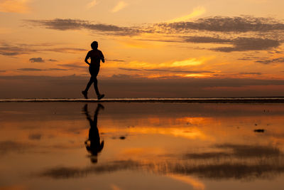 Silhouette man standing at beach against sky during sunset