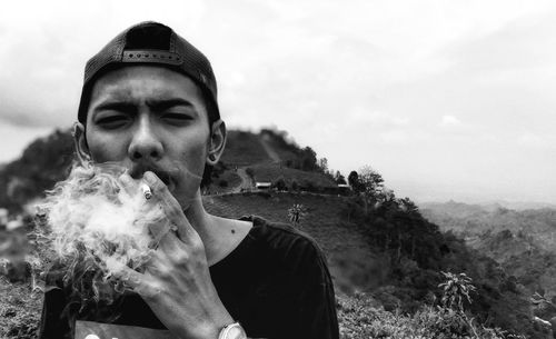 Portrait of man smoking cigarette against sky