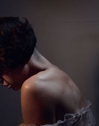 Side view of shirtless young woman sitting against black background