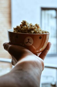 Cropped hand holding food in bowl at home