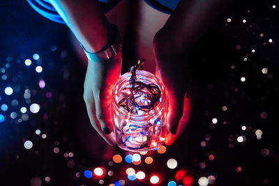 Low section of woman holding illuminated lights in jar at darkroom