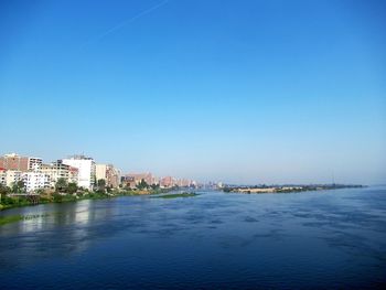 Scenic view of sea by buildings against clear blue sky