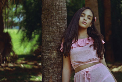 Portrait of young woman standing by tree trunk in forest