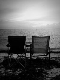 Chair on shore by sea against sky