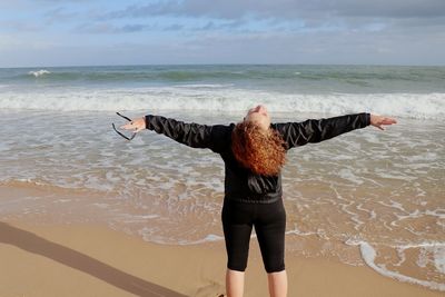 Rear view of man with arms raised on beach