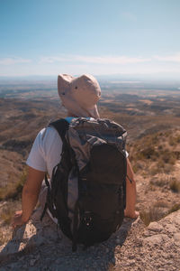 Rear view of man sitting on rock against sky