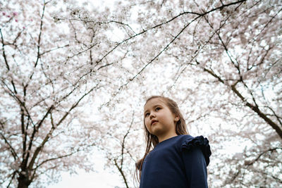 Low angle view of girl looking away against trees