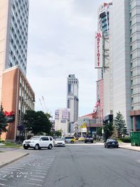 Cars on city street by buildings against sky