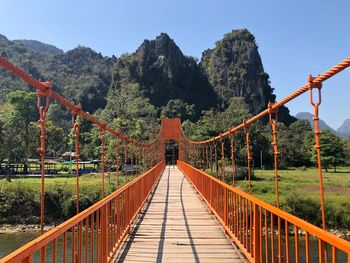 Footbridge amidst trees and mountains against sky