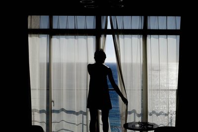 Silhouette of woman standing by window
