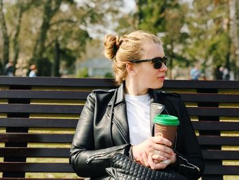 Young woman looking away while sitting on bench in park