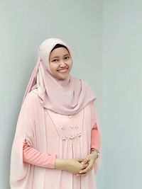 Portrait of young woman smiling while wearing hijab against wall