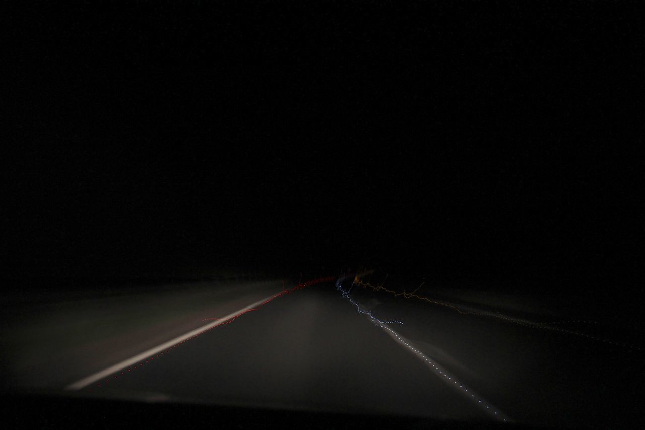 CLOSE-UP OF LIGHT TRAILS ON ROAD AGAINST BLACK BACKGROUND