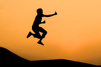 Full length of silhouette man jumping against orange sky