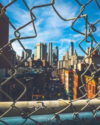 Cityscape seen through broken fence against sky