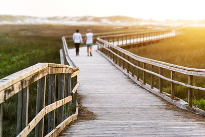 Rear view of friends walking on footbridge against sky