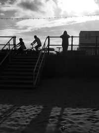 Silhouette people on steps by sea against sky