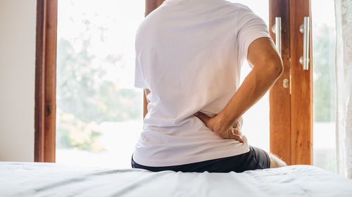 Rear view of man sitting on bed