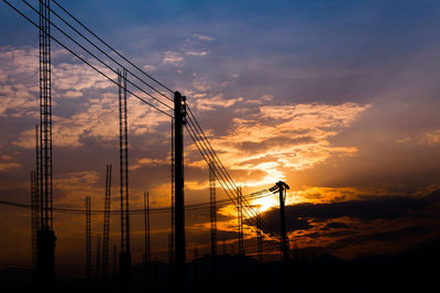 Low angle view of silhouette electricity pylon against dramatic sky