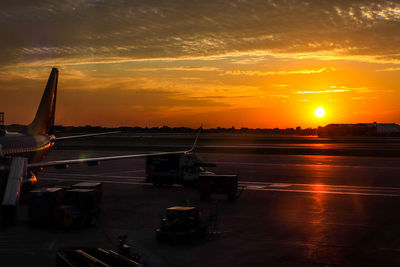 Airplane on runway against sky during sunset