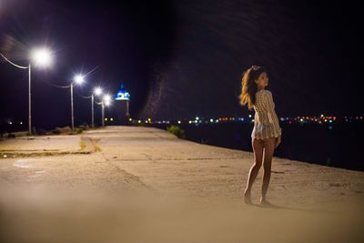 Woman walking on illuminated street at night